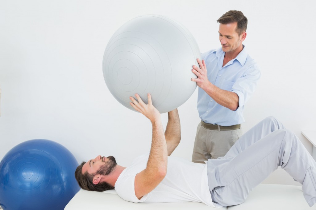 physical therapist helping patient do rehab with large ball